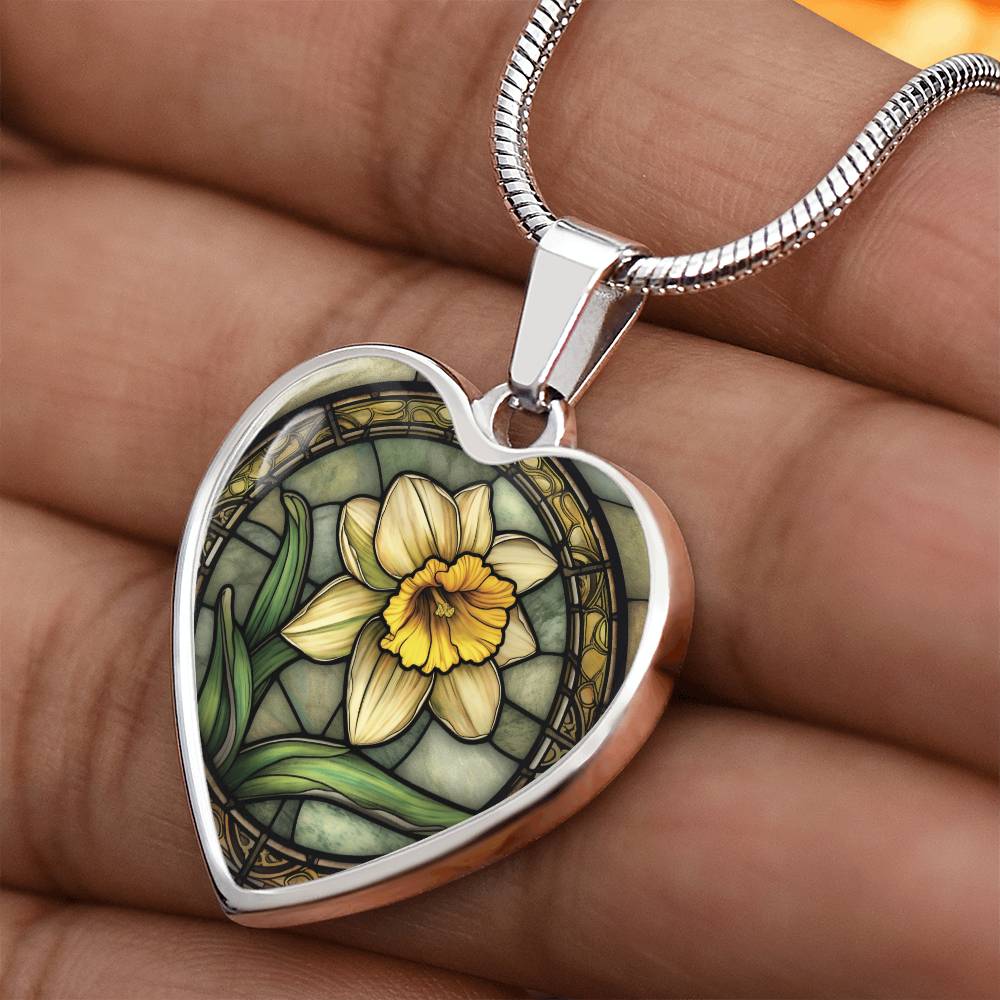 Woman holding an Elegant silver pendant featuring a vivid Daffodil Birth Flower Necklace, March birth month flower, set against a Green & Tan backdrop. This jewelry offers personalization with an engraving option for a name.