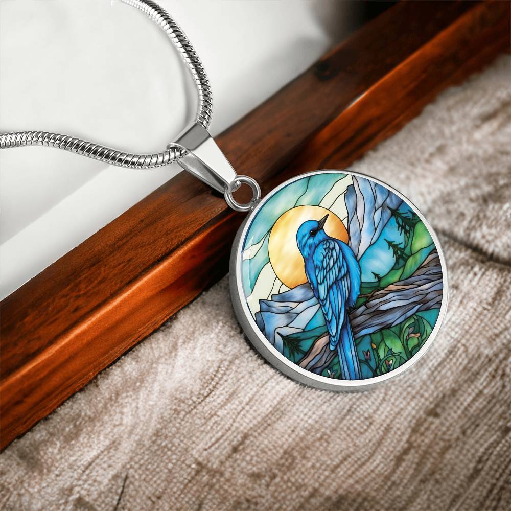 an Elegant silver pendant Blue Bird necklace. Colors blue bird and water, yellow sun, green trees and grass, brown branch, blue and white sky/ mountains. This jewelry offers personalization with an engraving option for a name.