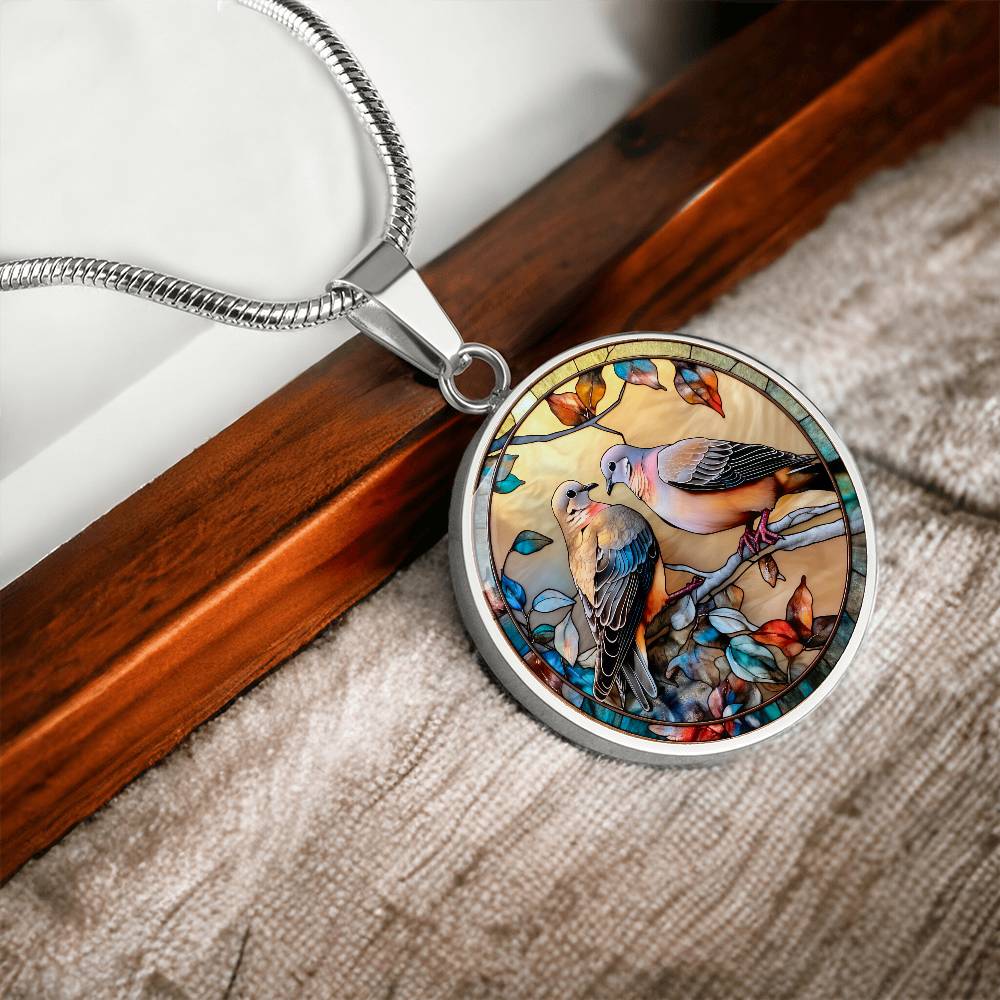 Elegant silver pendant necklace featuring two turtle doves, set against a subtle tan backdrop. This jewelry offers personalization with an engraving option for a name.