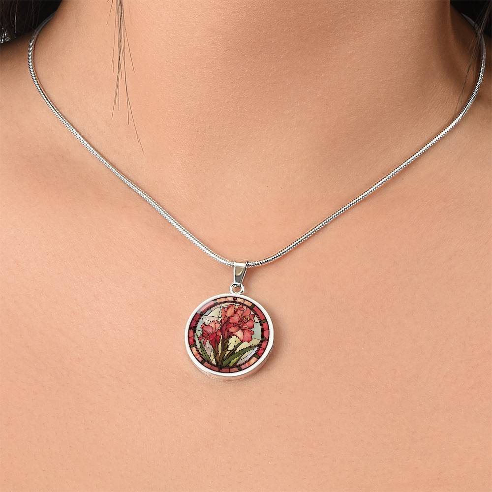 Woman wearing an elegant silver pendant Gladiolus Necklace. The colors are tan/green/blue/purple background, red and pink flowers, green grass, red border. This jewelry offers personalization with an engraving option for a name.
