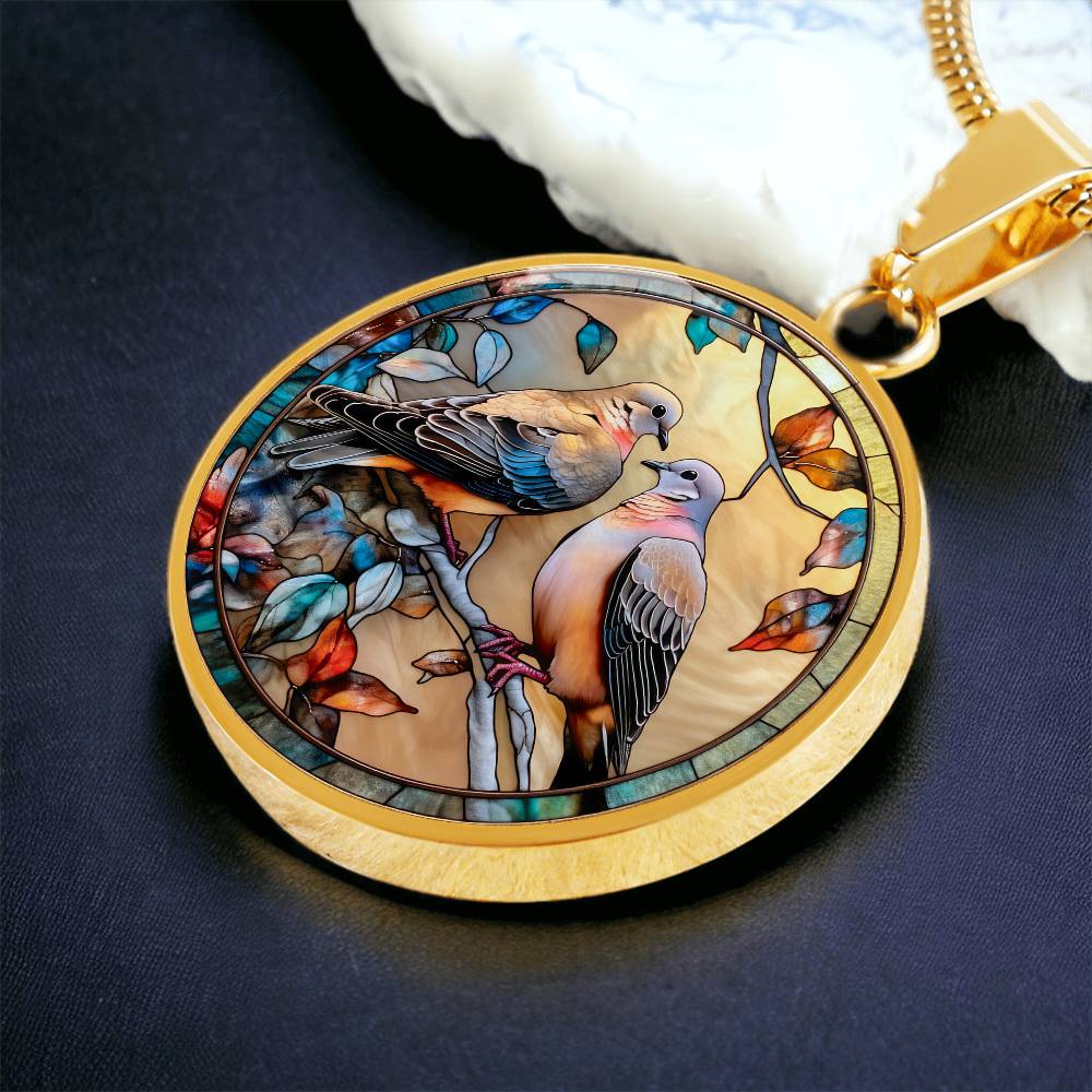 Elegant gold pendant necklace featuring two turtle doves, set against a subtle tan backdrop. This jewelry offers personalization with an engraving option for a name.