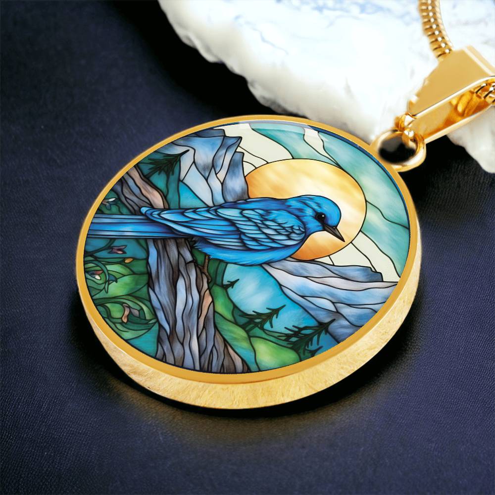 an Elegant gold pendant Blue Bird necklace. Colors blue bird and water, yellow sun, green trees and grass, brown branch, blue and white sky/ mountains. This jewelry offers personalization with an engraving option for a name.