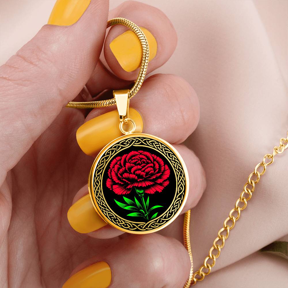 Woman holding an elegant Celtic gold pendant January Birth Flower Carnation necklace. A vivid red carnation, green stem & leaves, set against a gold & black backdrop. This jewelry offers personalization with an engraving option for a name.