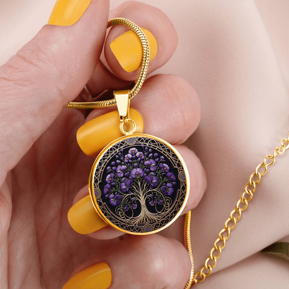 Woman holding an elegant gold pendant Larkspur Tree of Life Necklace. The Colors are purple, green and brown. This jewelry offers personalization with an engraving option for a name.