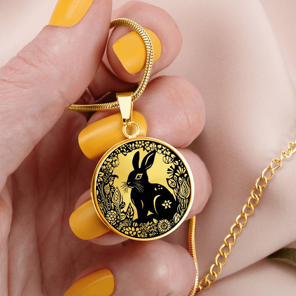 Woman holding an Elegant gold pendant Easter Bunny necklace featuring a bunny with leaves and flowers all in gold with a black background. This jewelry offers personalization with an engraving option for a name.