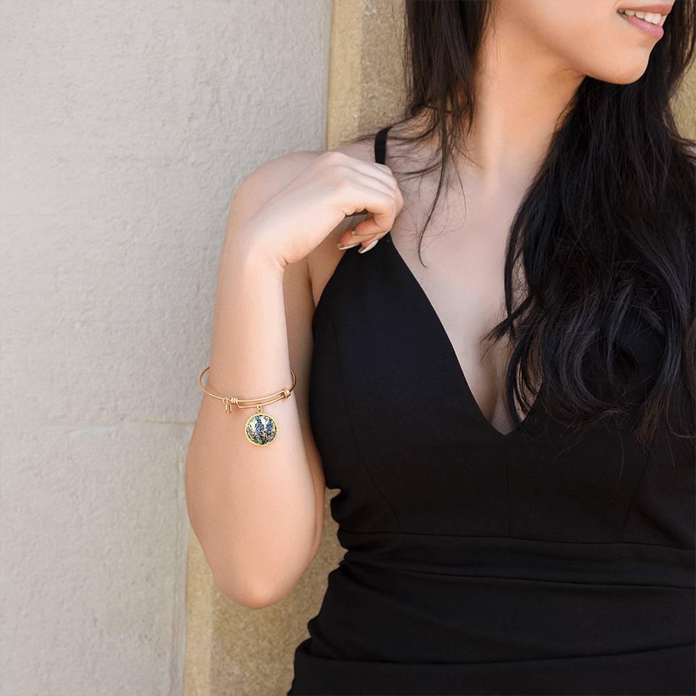 Woman wearing an elegant gold pendant Larkspur Flower Bracelet. The colors are blue, purple, green and tan. This jewelry offers personalization with an engraving option for a name.