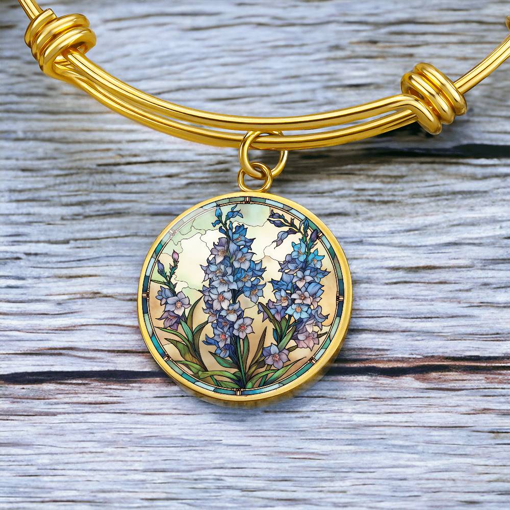An elegant Gold pendant Larkspur Flower Bracelet. The colors are blue, purple, green and tan. This jewelry offers personalization with an engraving option for a name.