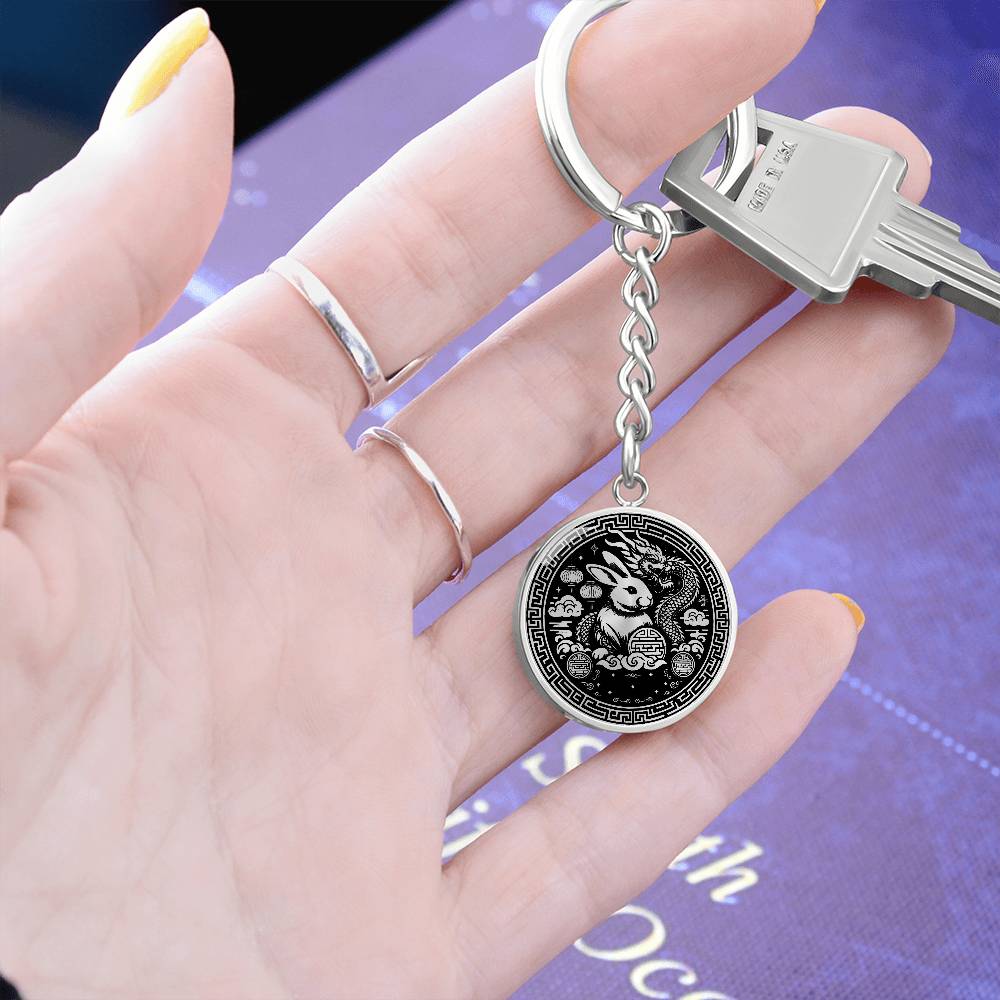 Woman holding a Year of the dragon keychain. Elegant silver pendant with a rabbit & dragon, is set against a silver backdrop. This jewelry offers personalization with an engraving option for a name.