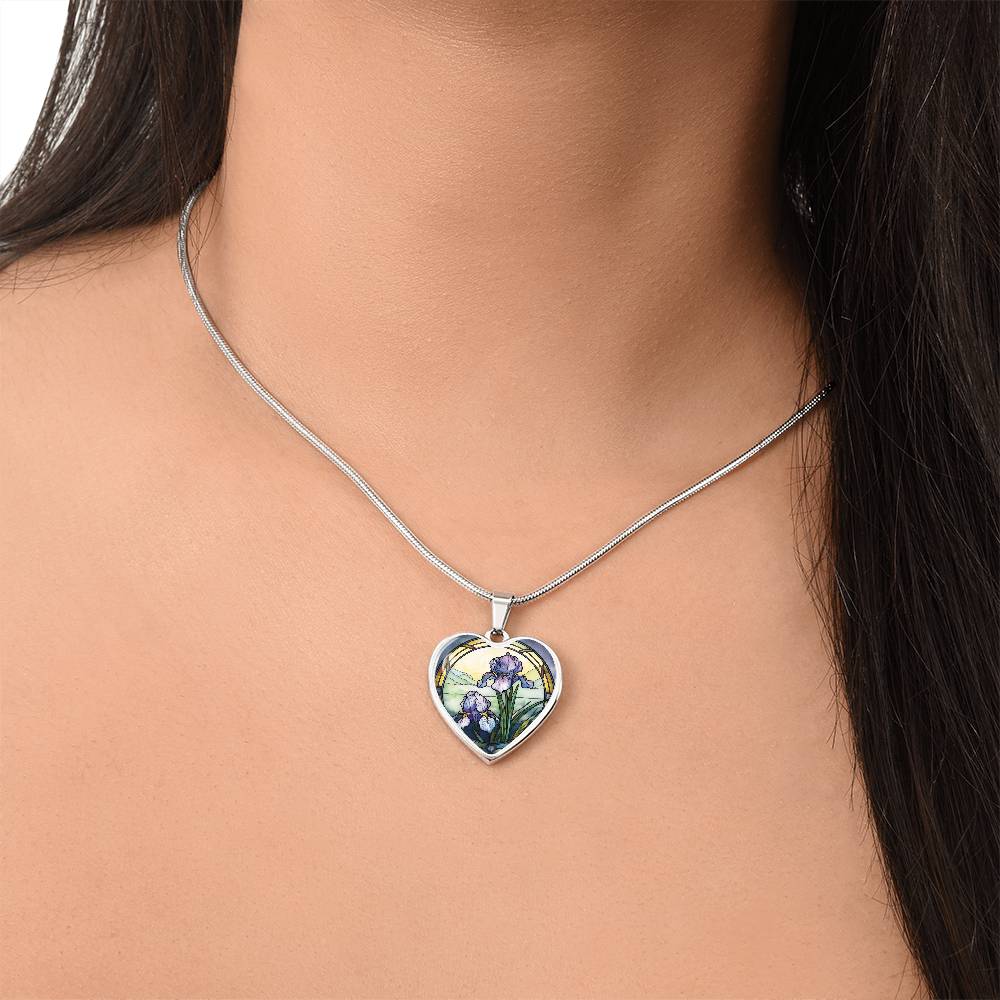 Woman wearing a Silver Heart Pendant Purple Iris flower necklace, With green grass, a Yellow sunset and Green mountains. This necklace offers personalization option for a name.