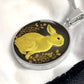 An Elegant silver pendant Rabbit Necklace. Yellow Rabbit and Flowers with a black and brown backdrop. This jewelry offers personalization with an engraving option for a name.