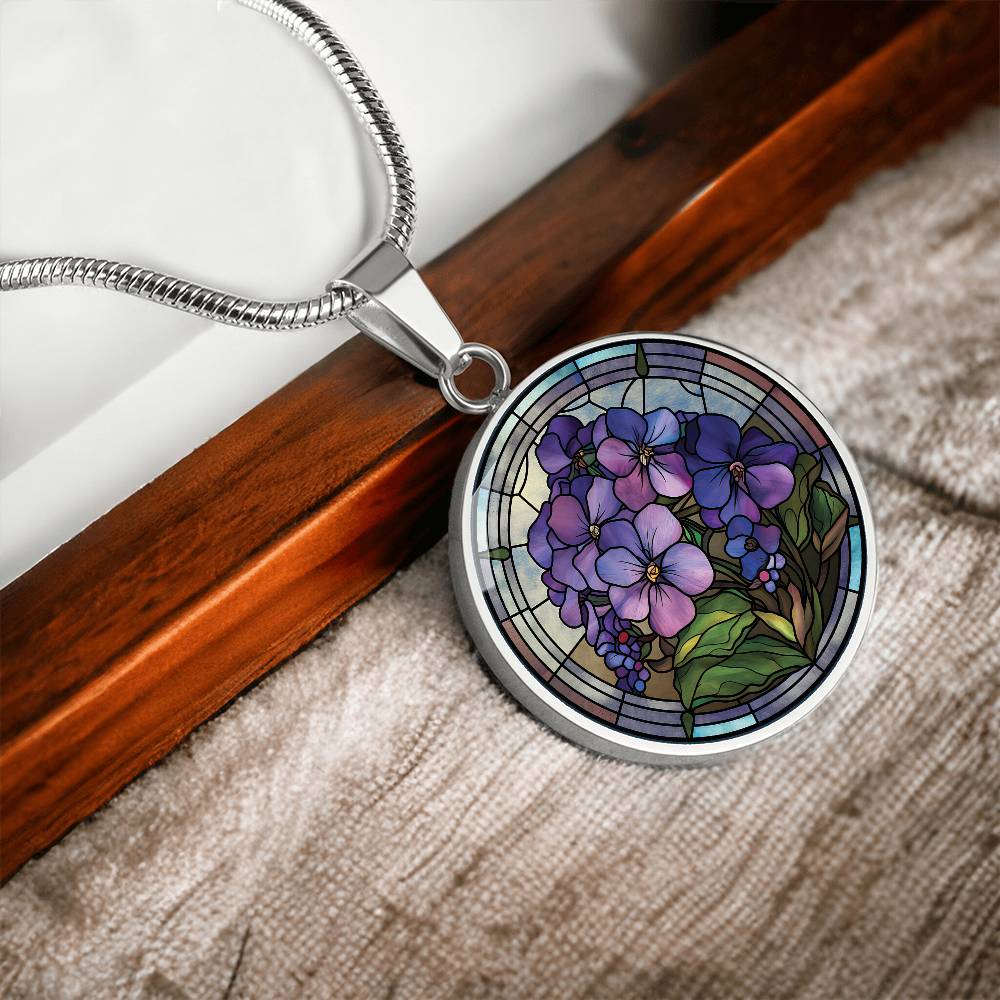 Elegant silver pendant African Violet Birth Flower Necklace. Violet and purple flowers, green grass, blue, purple, brown background. This jewelry offers personalization with an engraving option for a name.