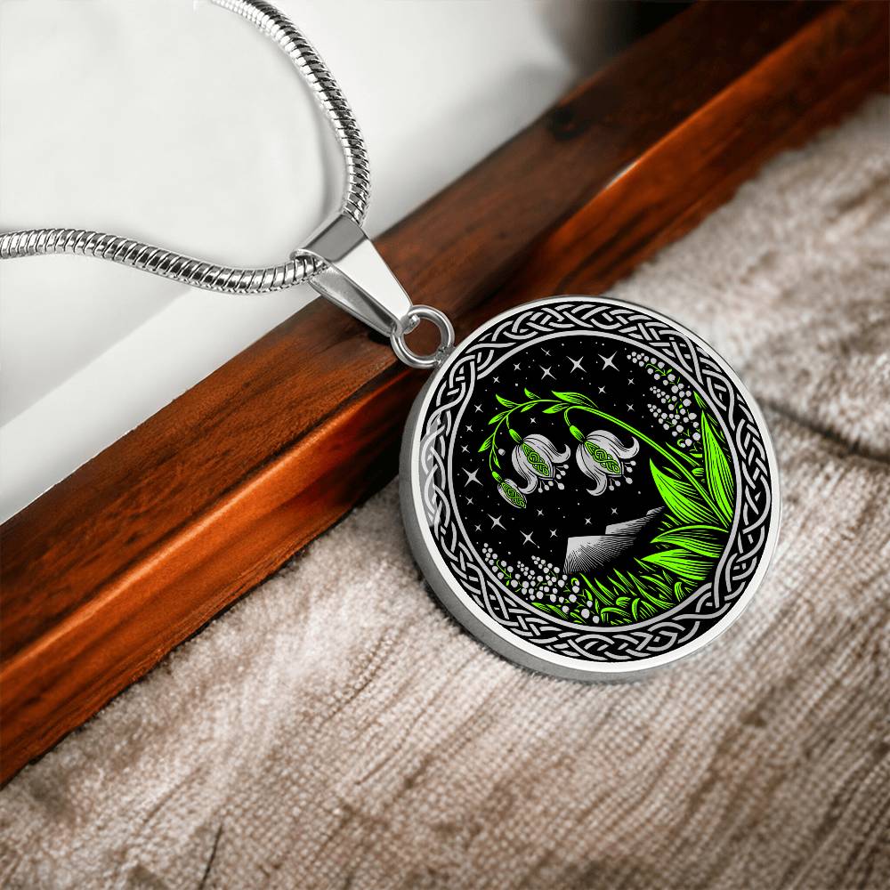 An Elegant silver pendant Celtic Lily Of The Valley Necklace featuring Green Grass, Silver Mountains, Stars,  Lily Of The Valleys, Celtic Knot Frame with a black backdrop. This jewelry offers personalization with an engraving option for a name.