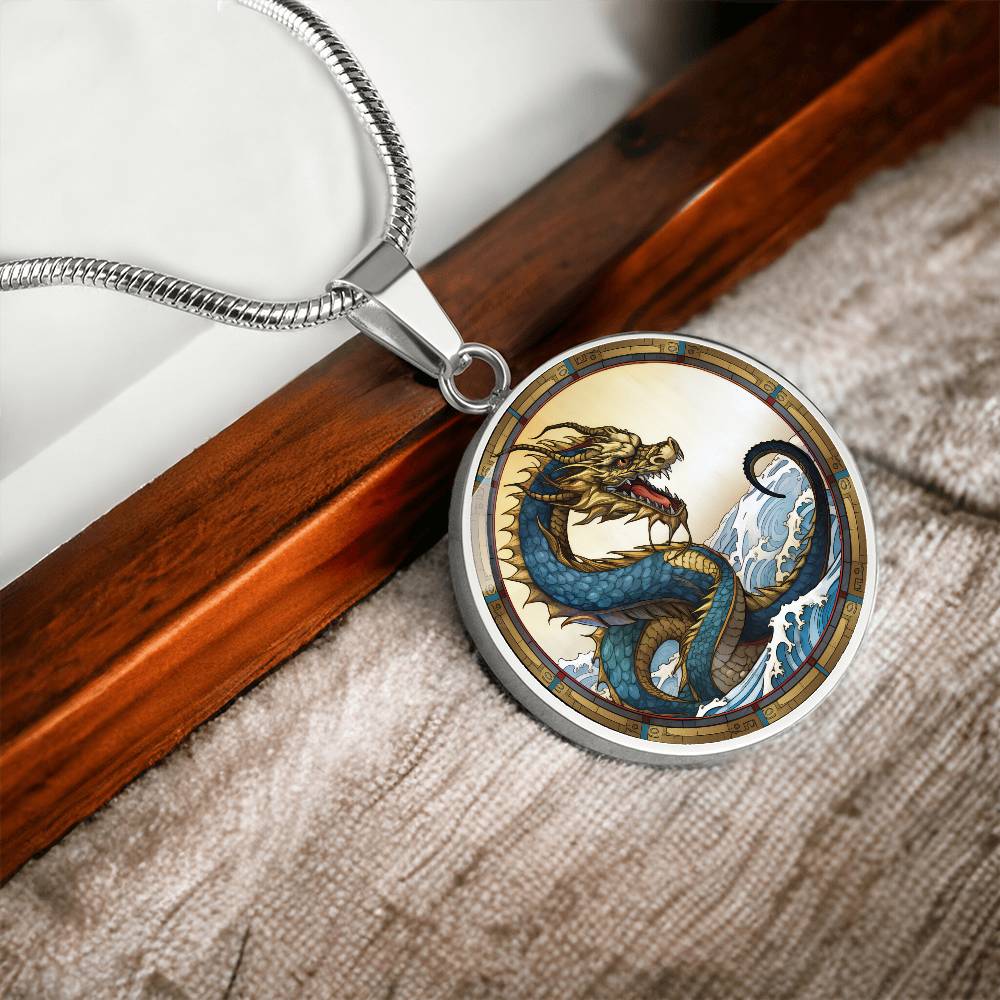 An Elegant silver pendant featuring a Water Dragon Necklace. Blue and yellow Dragon with a blue ocean, tan border and backdrop. This jewelry offers personalization with an engraving option for a name.