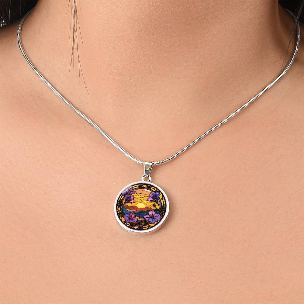 Woman wearing an elegant silver pendant Morning Glory Necklace. The colors are purple flowers, blue/green/purple hills, Brown mountains, Yellow sun and sky. This jewelry offers personalization with an engraving option for a name.