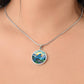 Woman wearing an Elegant silver pendant Blue Bird necklace. Colors blue bird and water, yellow sun, green trees and grass, brown branch, blue and white sky/ mountains. This jewelry offers personalization with an engraving option for a name.