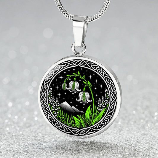 An Elegant silver pendant Celtic Lily Of The Valley Necklace featuring Green Grass, Silver Mountains, Stars,  Lily Of The Valleys, Celtic Knot Frame with a black backdrop. This jewelry offers personalization with an engraving option for a name.