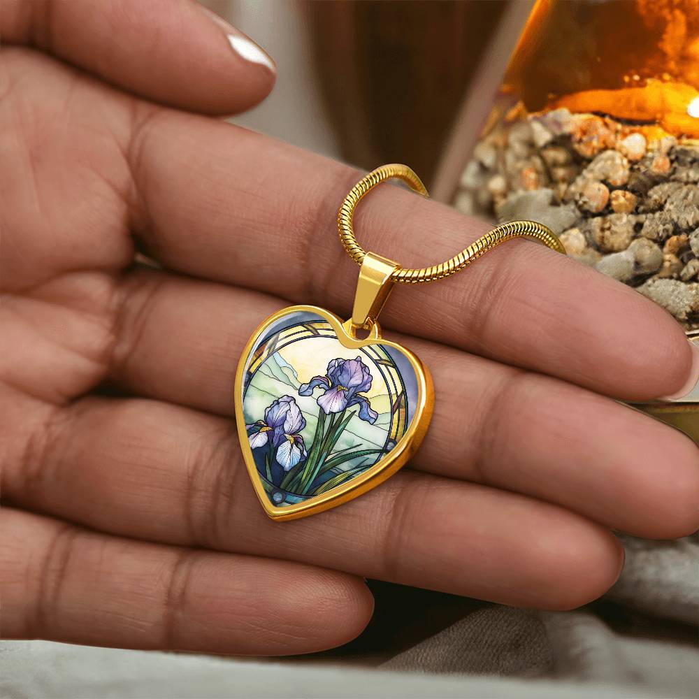 Woman holding a Gold Heart Pendant Purple Iris flower necklace, With green grass, a Yellow sunset and Green mountains. This necklace offers personalization option for a name.