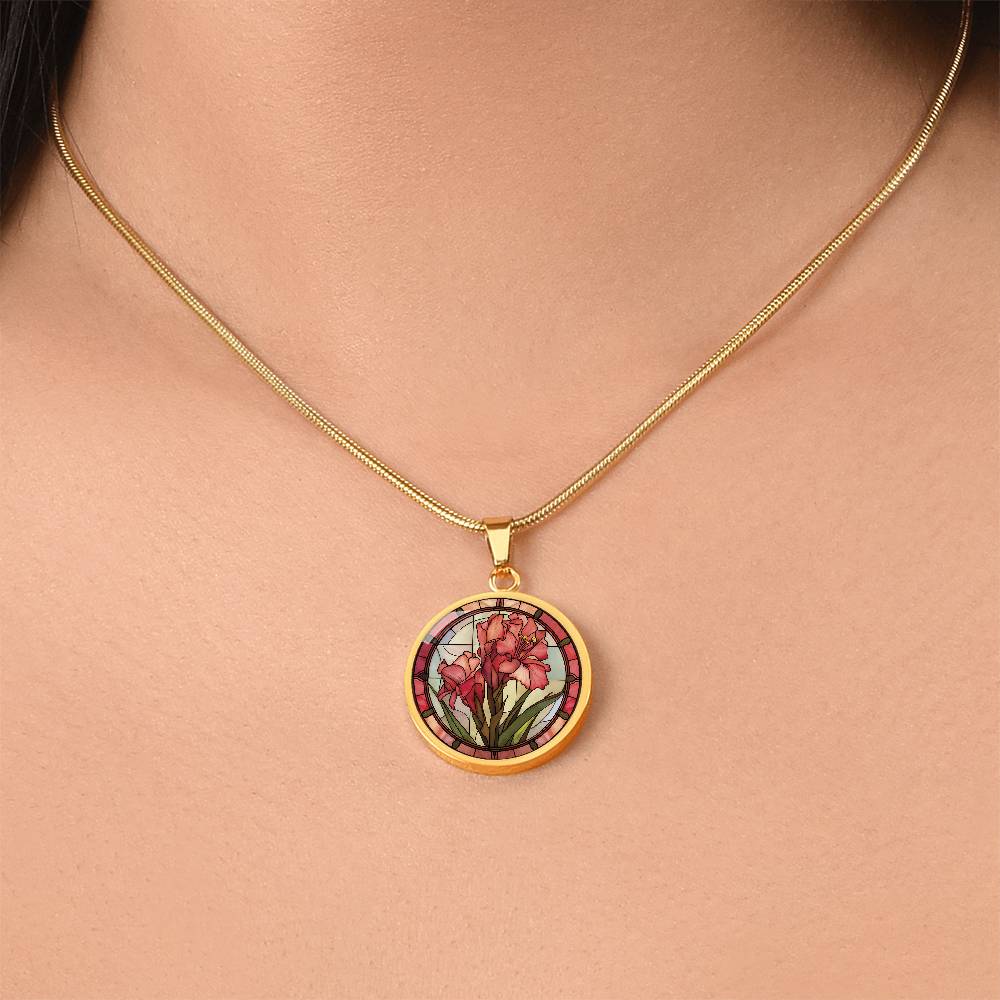 Woman wearing an elegant gold pendant Gladiolus Necklace. The colors are tan/green/blue/purple background, red and pink flowers, green grass, red border. This jewelry offers personalization with an engraving option for a name.