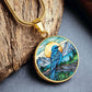 an Elegant gold pendant Blue Bird necklace. Colors blue bird and water, yellow sun, green trees and grass, brown branch, blue and white sky/ mountains. This jewelry offers personalization with an engraving option for a name.