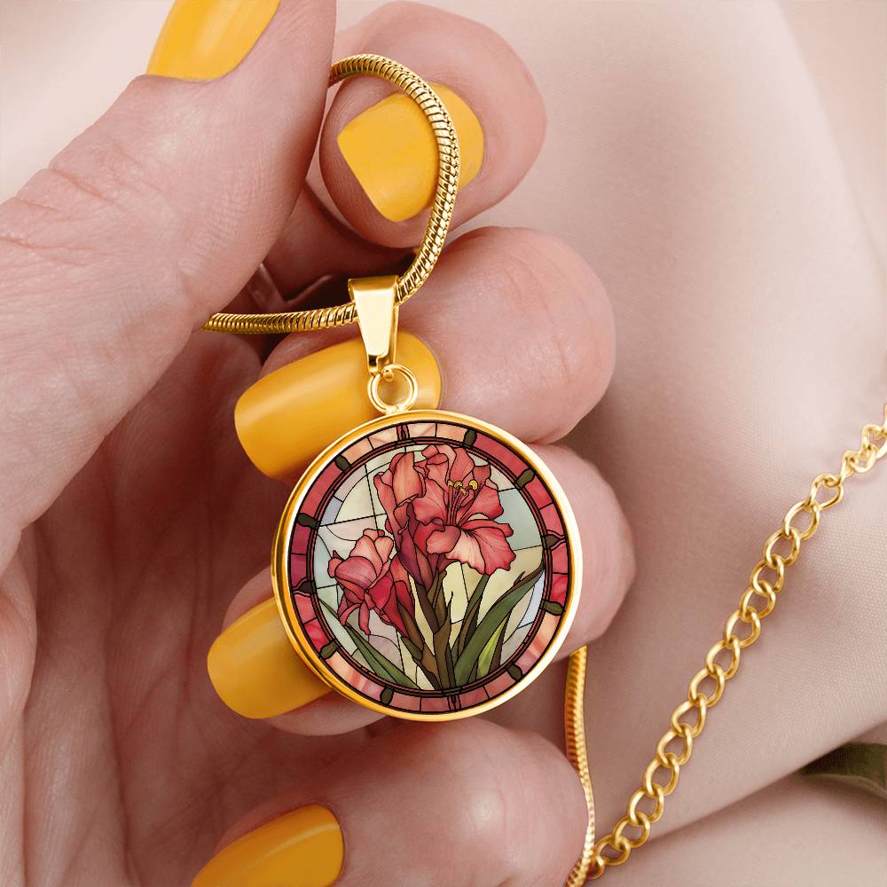 Woman holding an elegant gold pendant Gladiolus Necklace. The colors are tan/green/blue/purple background, red and pink flowers, green grass, red border. This jewelry offers personalization with an engraving option for a name.