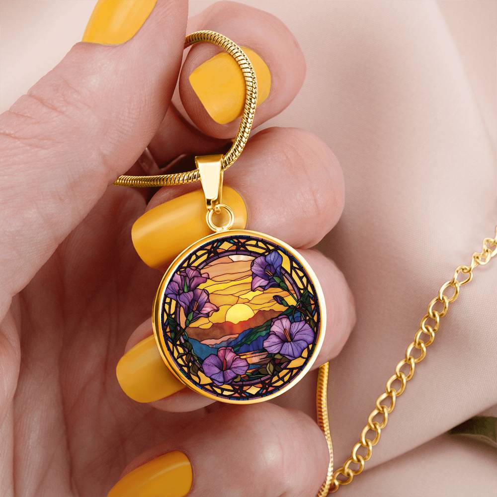 Woman holding an elegant gold pendant Morning Glory Necklace. The colors are purple flowers, blue/green/purple hills, Brown mountains, Yellow sun and sky. This jewelry offers personalization with an engraving option for a name.