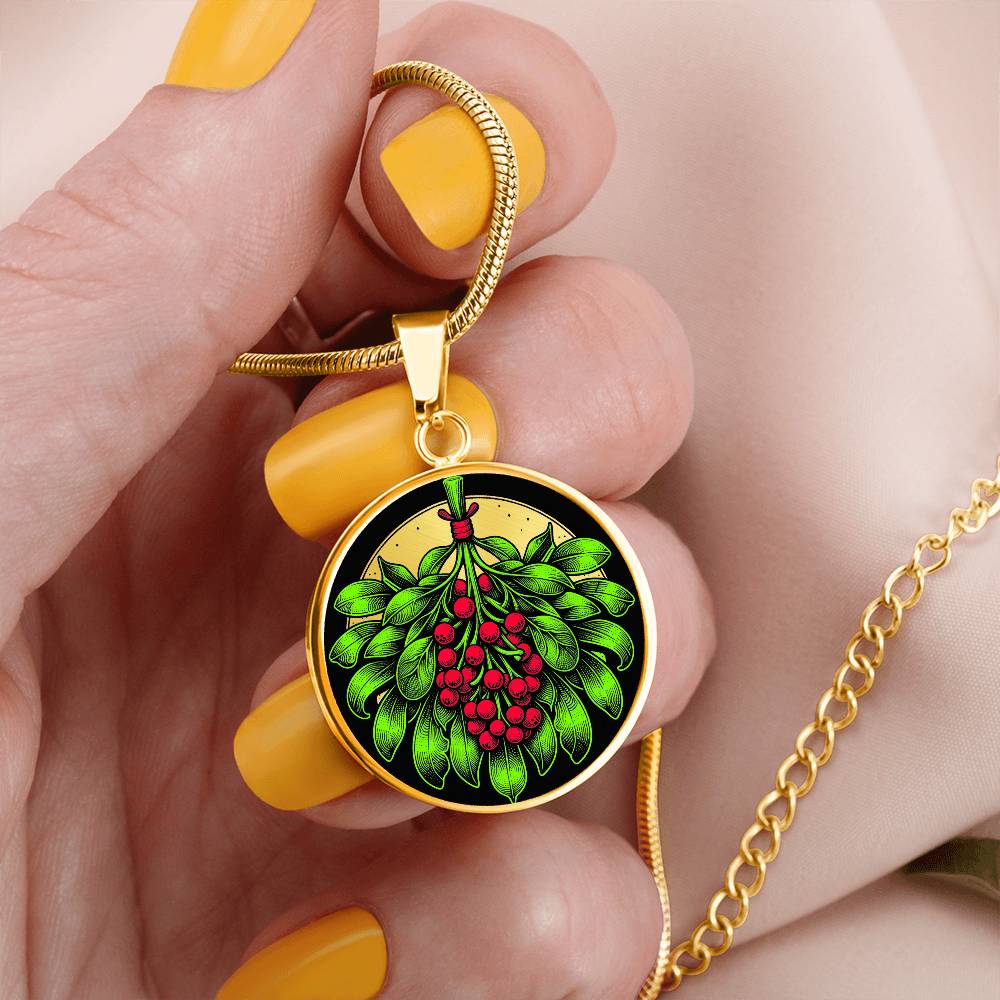 Woman holding an Elegant gold pendant necklace featuring a vivid Mistletoe with red berries set against a gold & black backdrop. This necklace offers personalization with an engraving option for a name.