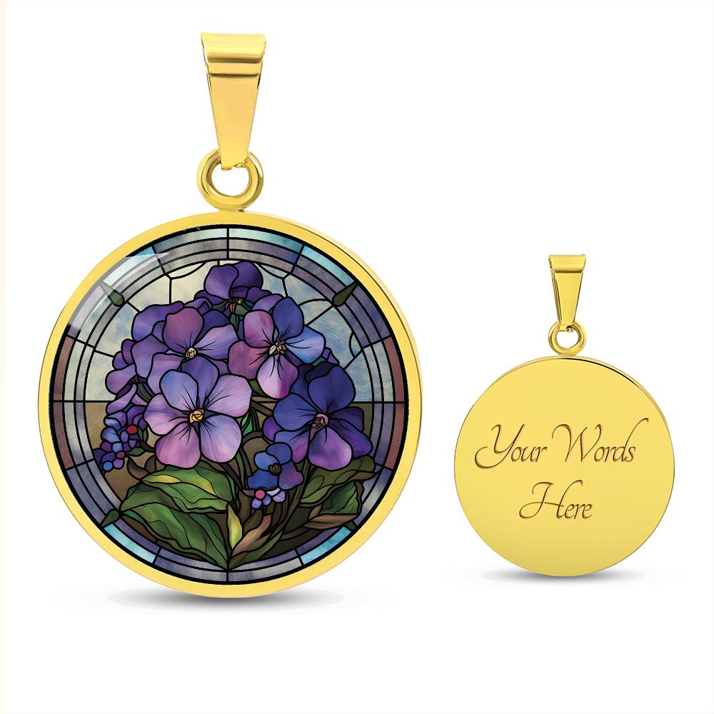 an Elegant gold pendant African Violet Birth Flower Necklace. Violet and purple flowers, green grass, blue, purple, brown background. This jewelry offers personalization with an engraving option for a name.