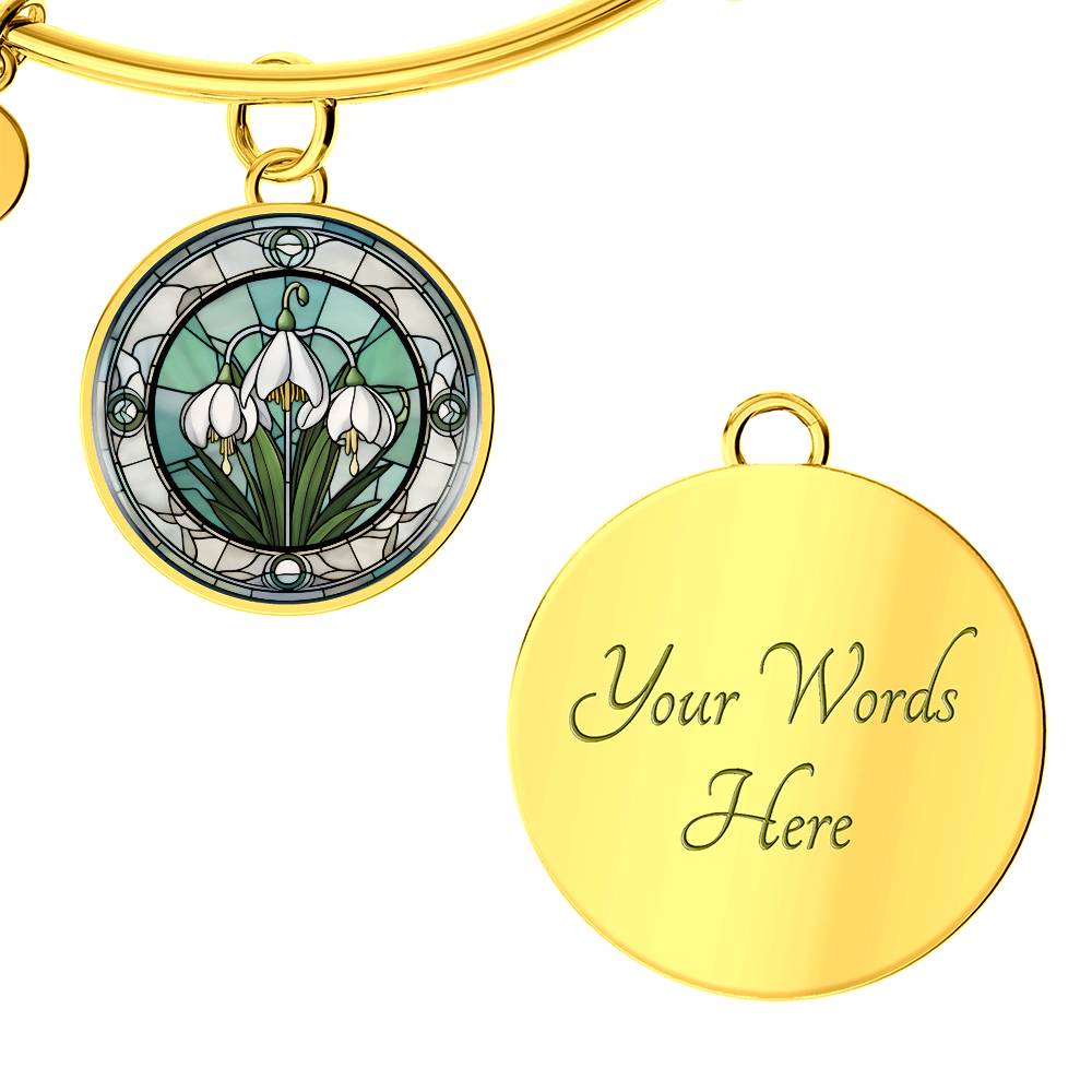 an Elegant gold pendant Snowdrop Flower Bracelet, Januarys birth month flower, set against a subtle green and grey backdrop. This jewelry offers personalization with an engraving option for a name.