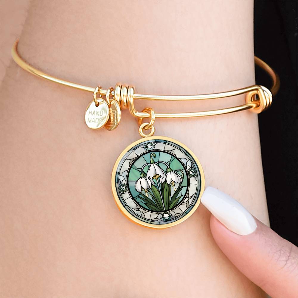 Woman wearing an Elegant gold pendant Snowdrop Flower Bracelet, Januarys birth month flower, set against a subtle green and grey backdrop. This jewelry offers personalization with an engraving option for a name.