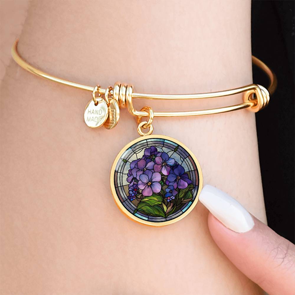 Woman wearing an Elegant gold pendant featuring a purple African Violet Birth Flower Bracelet, February&#39;s birth month flower, set against a blue and brown backdrop. This jewelry offers personalization with an engraving option for a name.