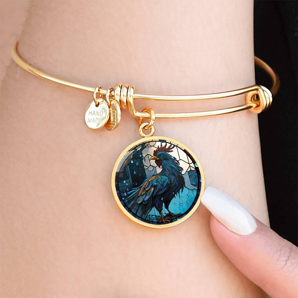 Woman wearing an Elegant gold pendant Rooster Bracelet, featuring a blue/red colored rooster set against a tan/blue Rain backdrop. This jewelry offers personalization with an engraving option for a name.