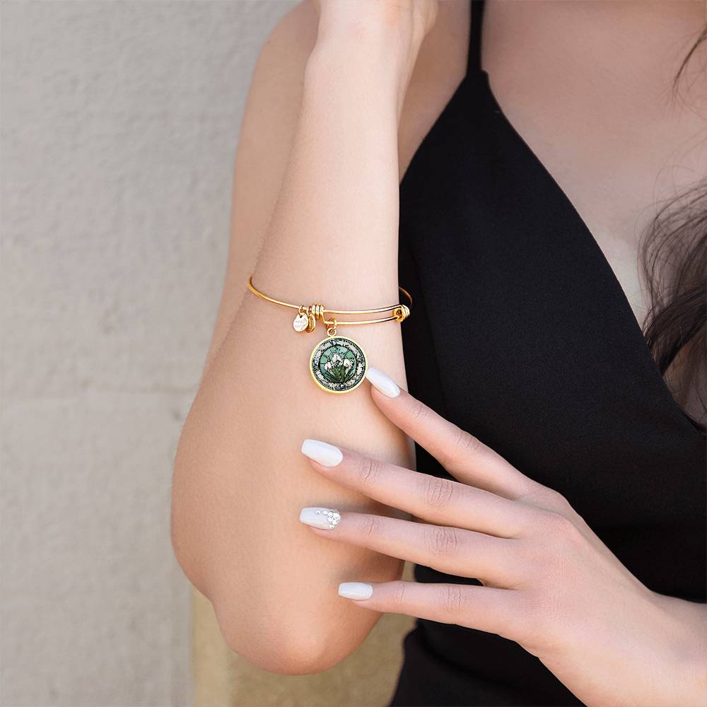 Woman wearing an Elegant gold pendant Snowdrop Flower Bracelet, Januarys birth month flower, set against a subtle green and grey backdrop. This jewelry offers personalization with an engraving option for a name.