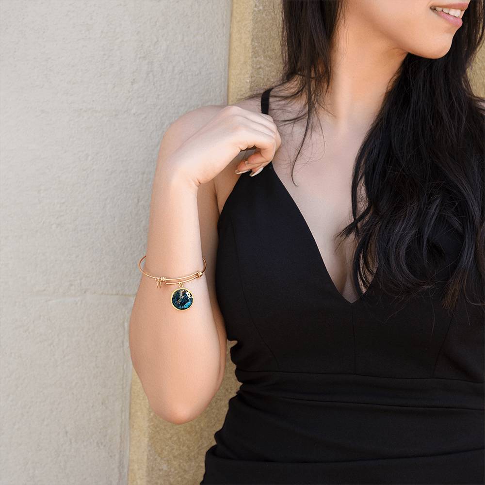 Woman wearing an Elegant gold pendant Rooster Bracelet, featuring a blue/red colored rooster set against a tan/blue Rain backdrop. This jewelry offers personalization with an engraving option for a name.