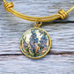An elegant Gold pendant Larkspur Flower Bracelet. The colors are blue, purple, green and tan. This jewelry offers personalization with an engraving option for a name.