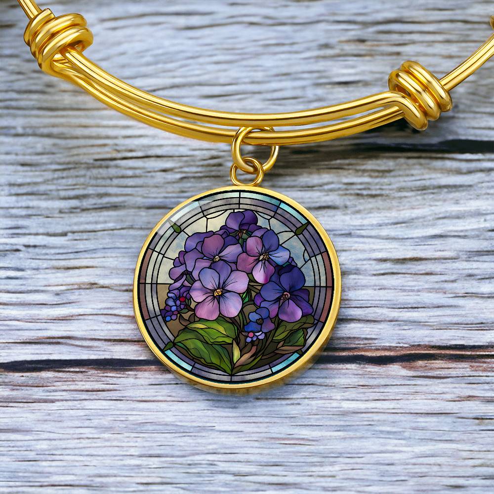 an Elegant gold pendant featuring a purple African Violet Birth Flower Bracelet, February&#39;s birth month flower, set against a blue and brown backdrop. This jewelry offers personalization with an engraving option for a name.