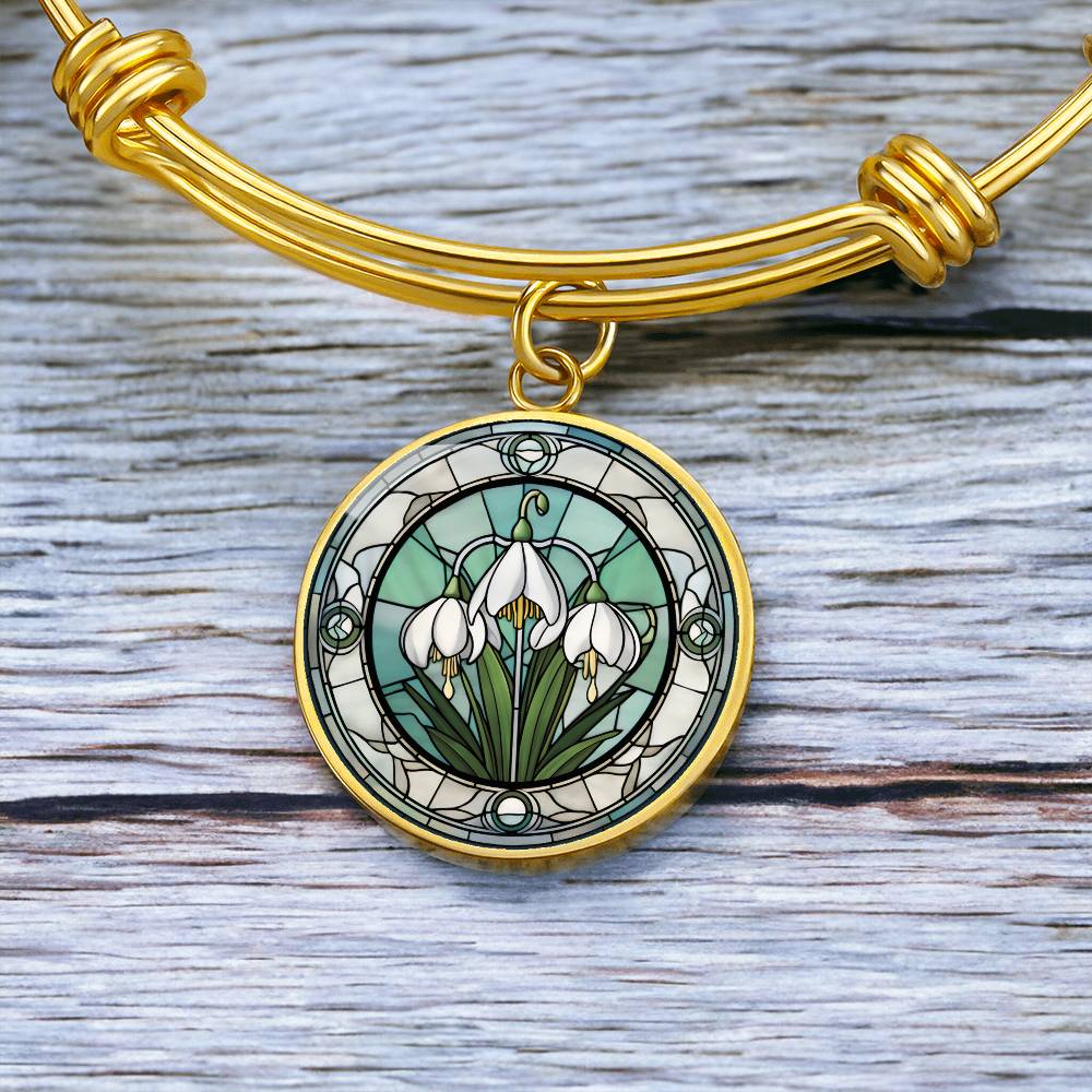 an Elegant gold pendant Snowdrop Flower Bracelet, Januarys birth month flower, set against a subtle green and grey backdrop. This jewelry offers personalization with an engraving option for a name.