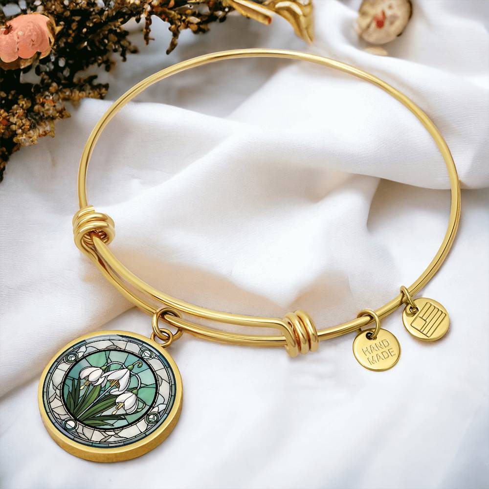 an Elegant gold pendant Snowdrop Flower Bracelet, Januarys birth month flower, set against a subtle green and grey backdrop. This jewelry offers personalization with an engraving option for a name.