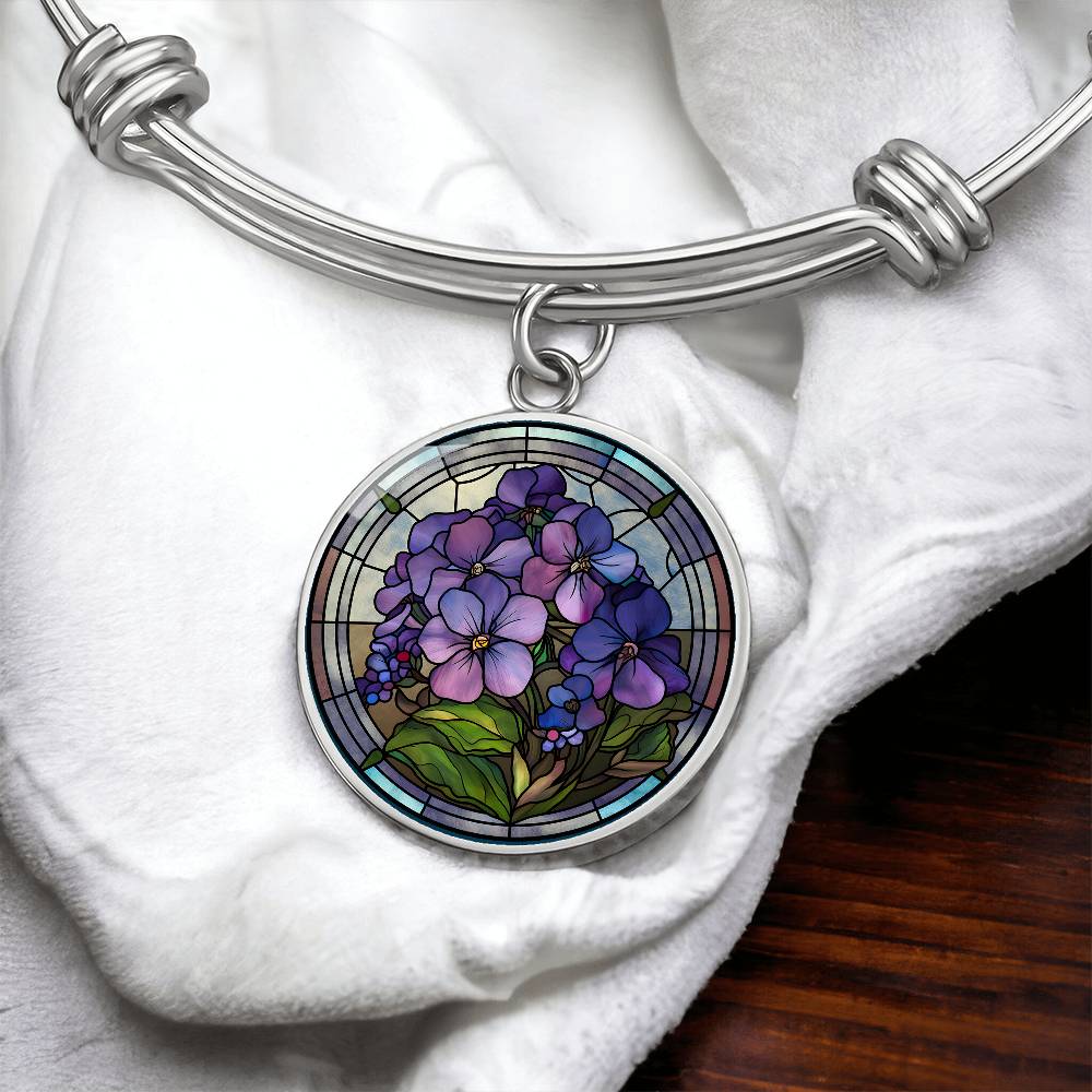 an Elegant silver pendant featuring a purple African Violet Birth Flower Bracelet, February&#39;s birth month flower, set against a blue and brown backdrop. This jewelry offers personalization with an engraving option for a name.