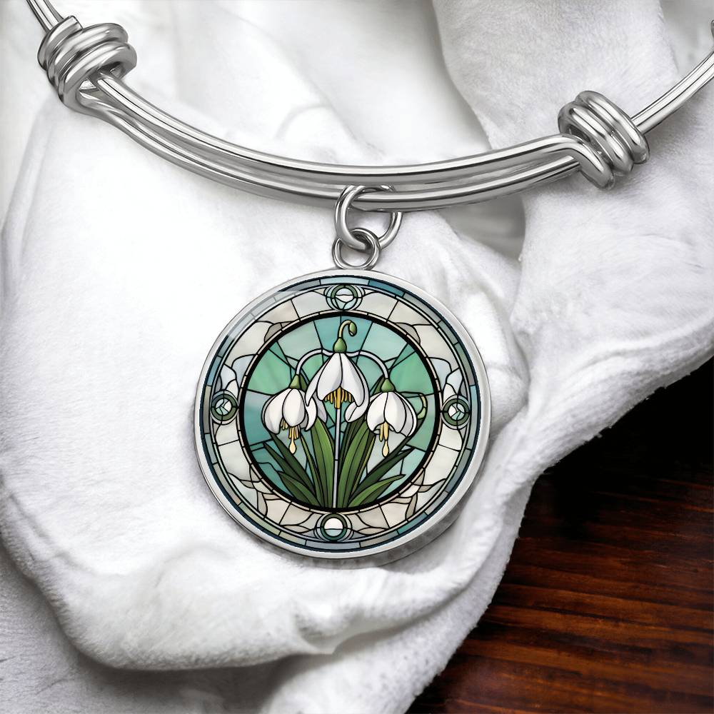 an Elegant silver pendant Snowdrop Flower Bracelet, Januarys birth month flower, set against a subtle green and grey backdrop. This jewelry offers personalization with an engraving option for a name.