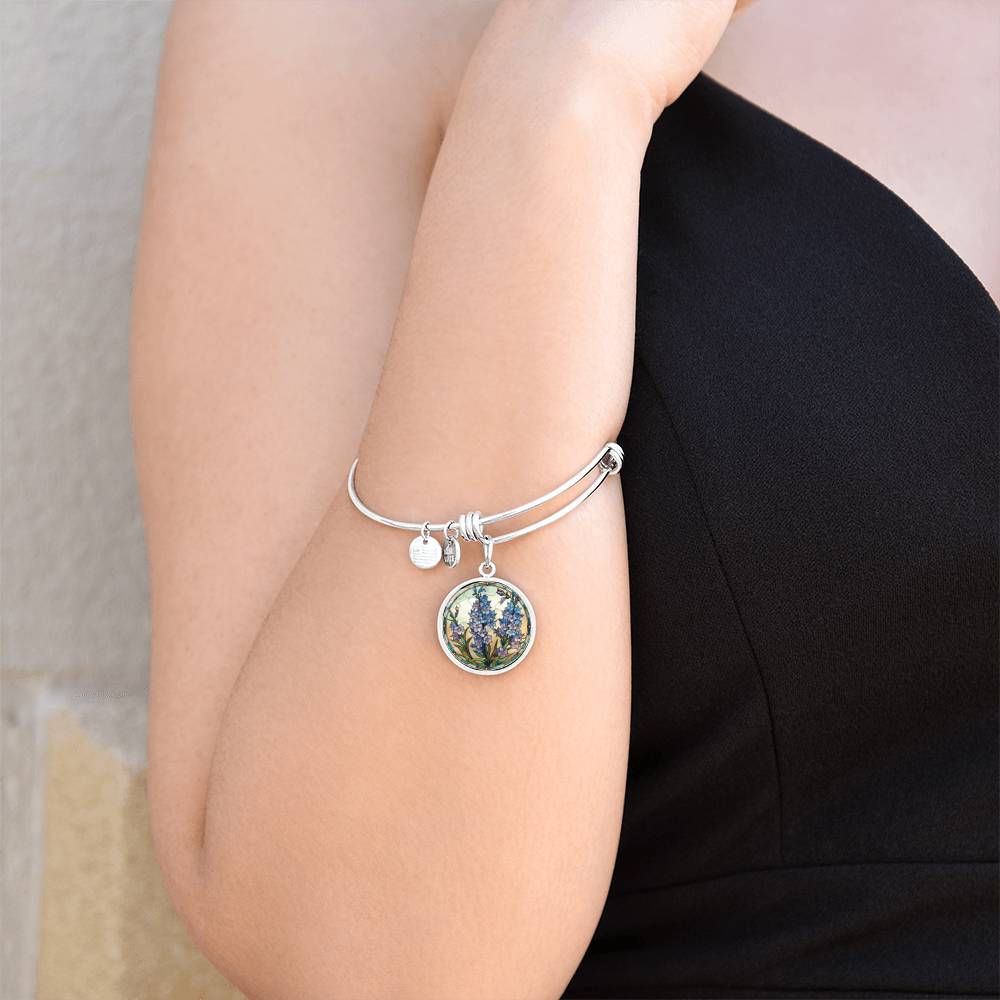 Woman wearing an elegant silver pendant Larkspur Flower Bracelet. The colors are blue, purple, green and tan. This jewelry offers personalization with an engraving option for a name.