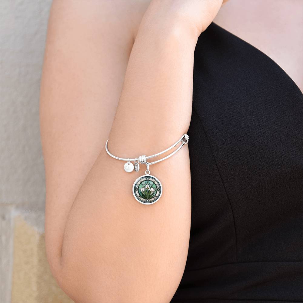 Woman wearing an Elegant silver pendant Snowdrop Flower Bracelet, Januarys birth month flower, set against a subtle green and grey backdrop. This jewelry offers personalization with an engraving option for a name.