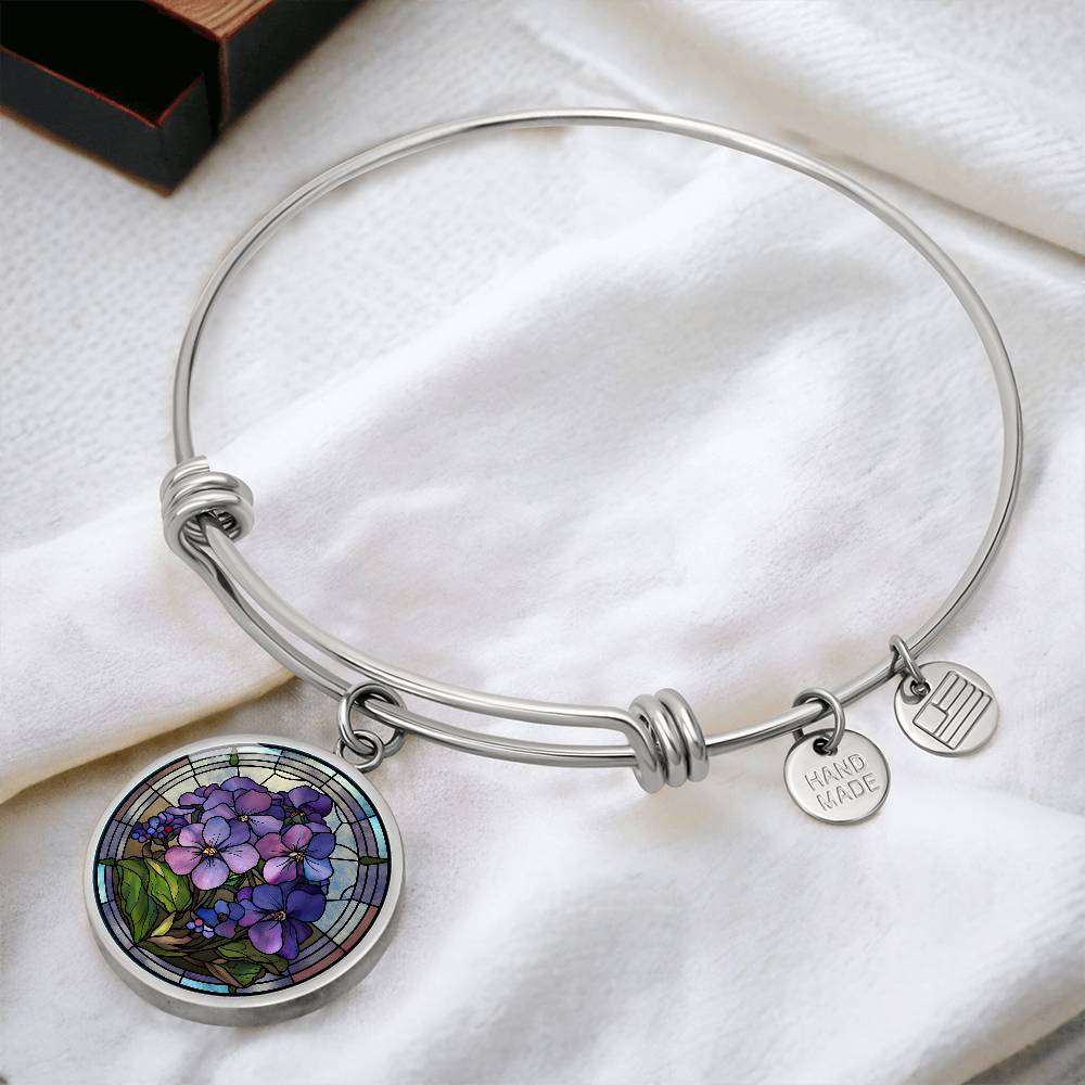 an Elegant silver pendant featuring a purple African Violet Birth Flower Bracelet, February&#39;s birth month flower, set against a blue and brown backdrop. This jewelry offers personalization with an engraving option for a name.