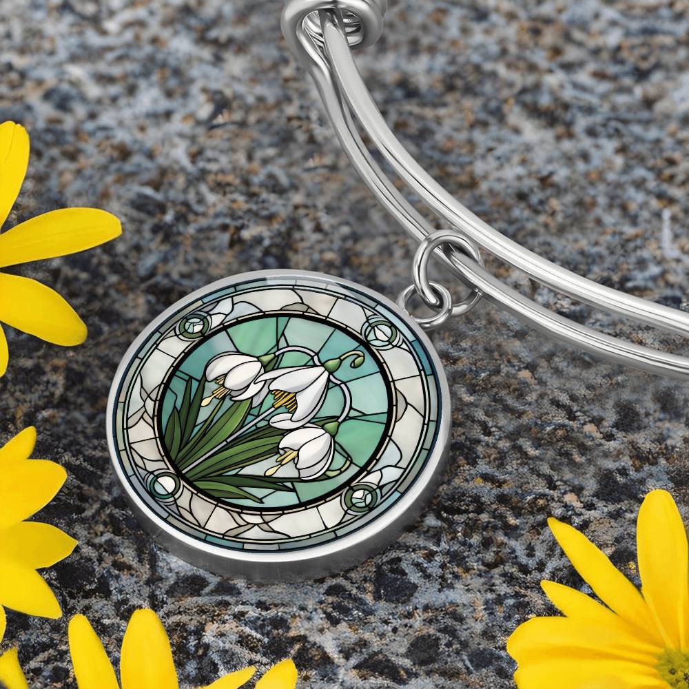 an Elegant silver pendant Snowdrop Flower Bracelet, Januarys birth month flower, set against a subtle green and grey backdrop. This jewelry offers personalization with an engraving option for a name.