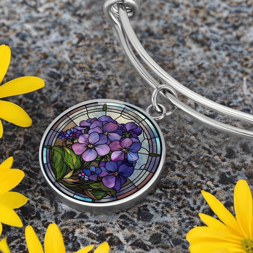 an Elegant silver pendant featuring a purple African Violet Birth Flower Bracelet, February&#39;s birth month flower, set against a blue and brown backdrop. This jewelry offers personalization with an engraving option for a name.