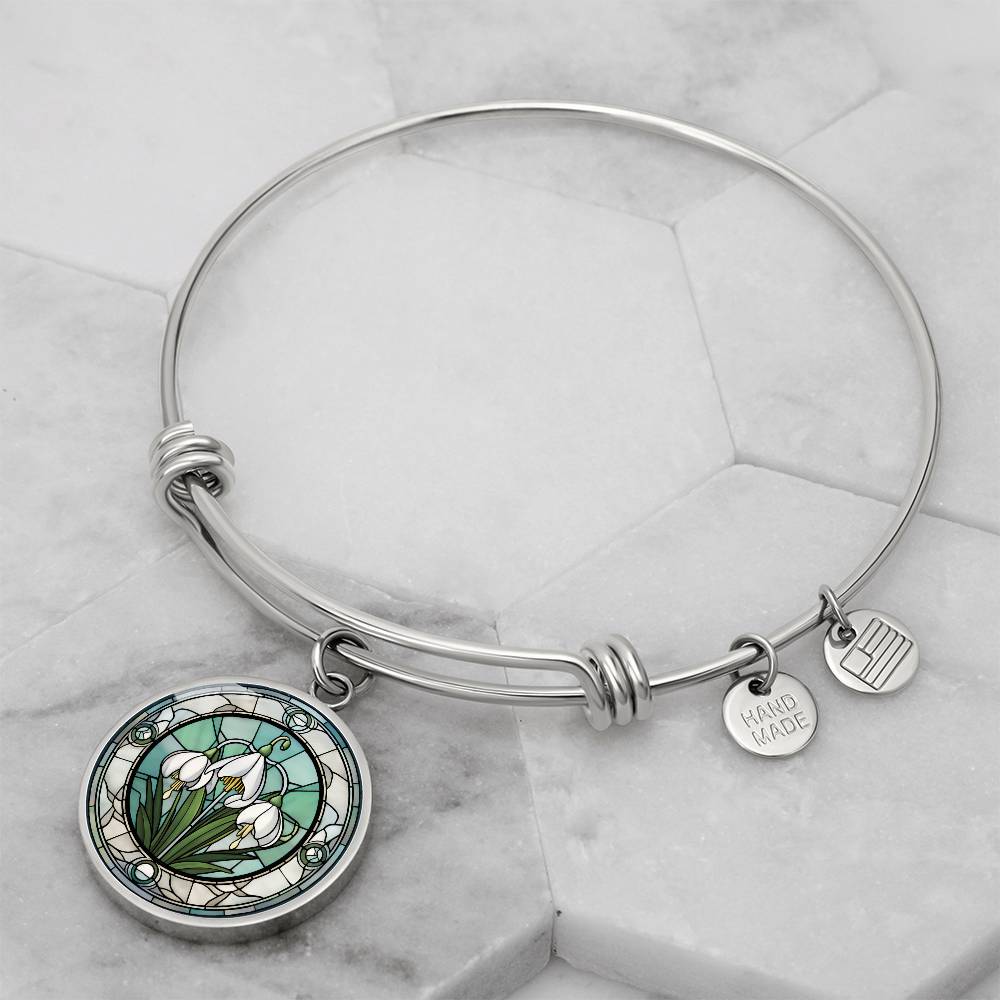 an Elegant silver pendant Snowdrop Flower Bracelet, Januarys birth month flower, set against a subtle green and grey backdrop. This jewelry offers personalization with an engraving option for a name.