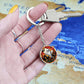Woman holding an elegant silver pendant Halloween Ghost Keychain. The colors are white, black, yellow, orange and green. This jewelry offers personalization with an engraving option for a name.