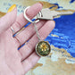 Woman holding An Elegant Silver pendant Daffodil Necklace, March&#39;s birth month flower. Colors, Yellow flower, Green Grass, Brown Border, Dark Green background. This jewelry offers personalization with an engraving option for a name.