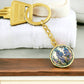An elegant gold pendant Larkspur Flower Keychain. The colors are blue, purple, green and tan. This jewelry offers personalization with an engraving option for a name.