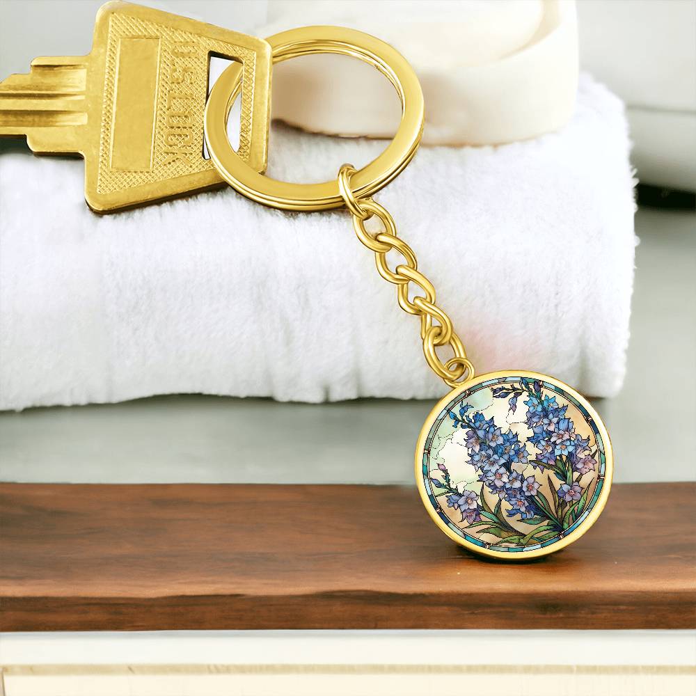 An elegant gold pendant Larkspur Flower Keychain. The colors are blue, purple, green and tan. This jewelry offers personalization with an engraving option for a name.