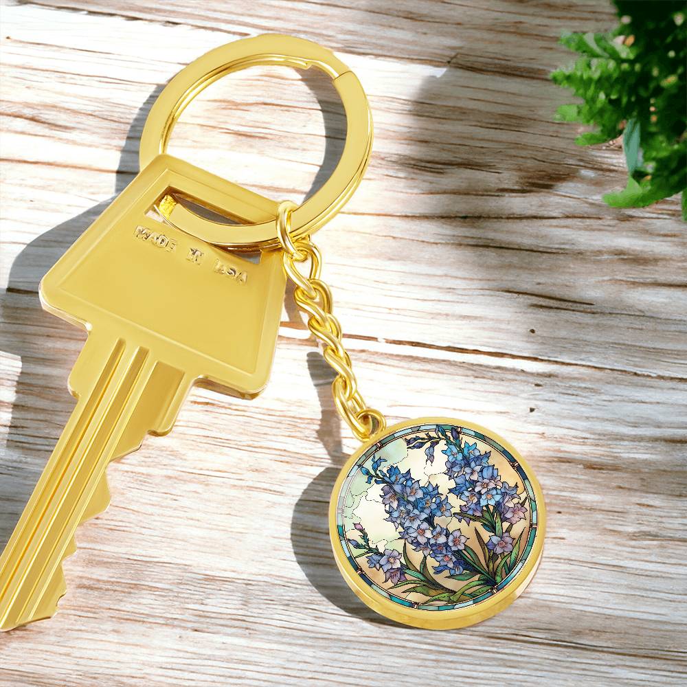 An elegant gold pendant Larkspur Flower Keychain. The colors are blue, purple, green and tan. This jewelry offers personalization with an engraving option for a name.